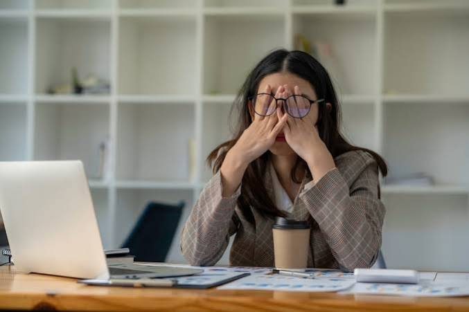 A woman at her desk resting her hands over her eyes, exhausted