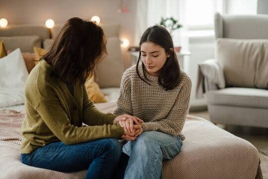 A parent sitting with their teenage daughter, holding her hands